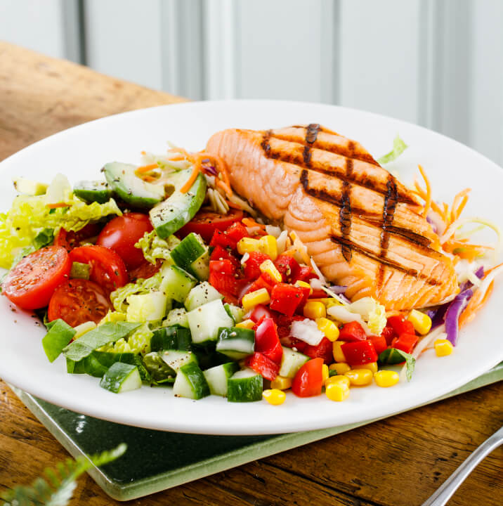 Beefeater grilled salmon on a bed of green lettuce, cucumber, cherry tomatoes, sweetcorn and peppers in a white dish.